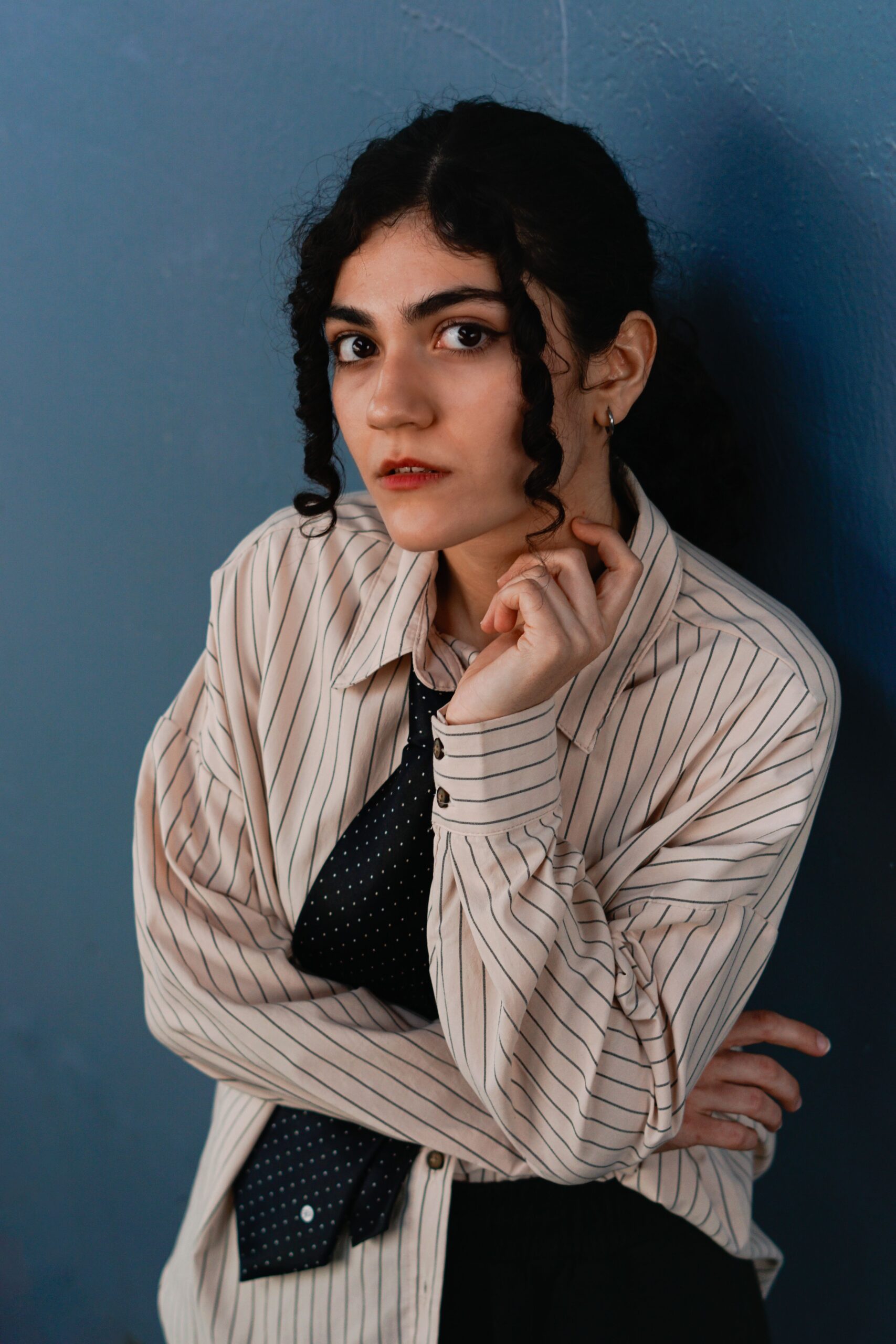 Portrait of an elegant woman with curly hair in a striped shirt and tie, posing in a studio setting.